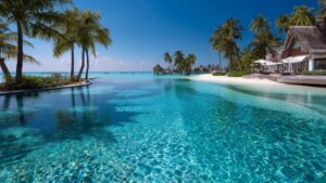 Luxury travel image of a stunning tropical resort with an infinity pool leading into the turquoise ocean and palm trees